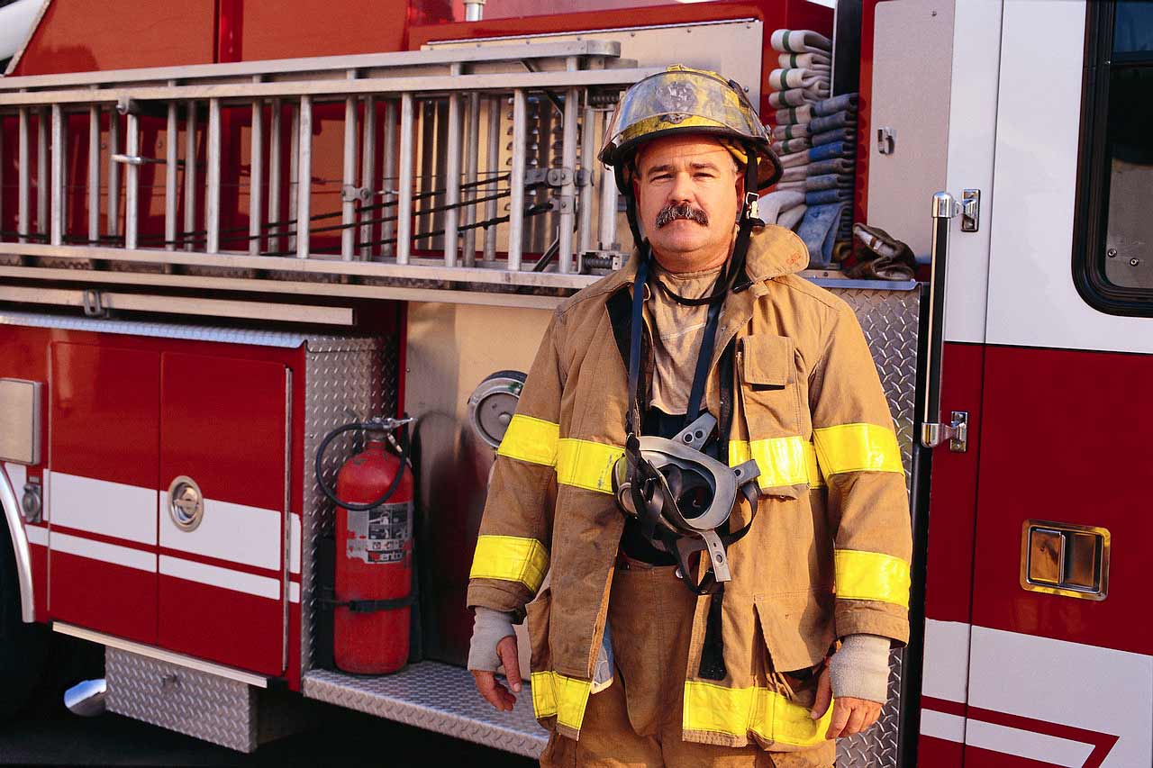 Lalaking bumbero na nakatayo sa harap ng isang fire engine.